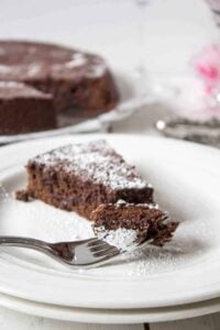 A slice of chocolate cake sprinkled with powdered sugar on a white plate.