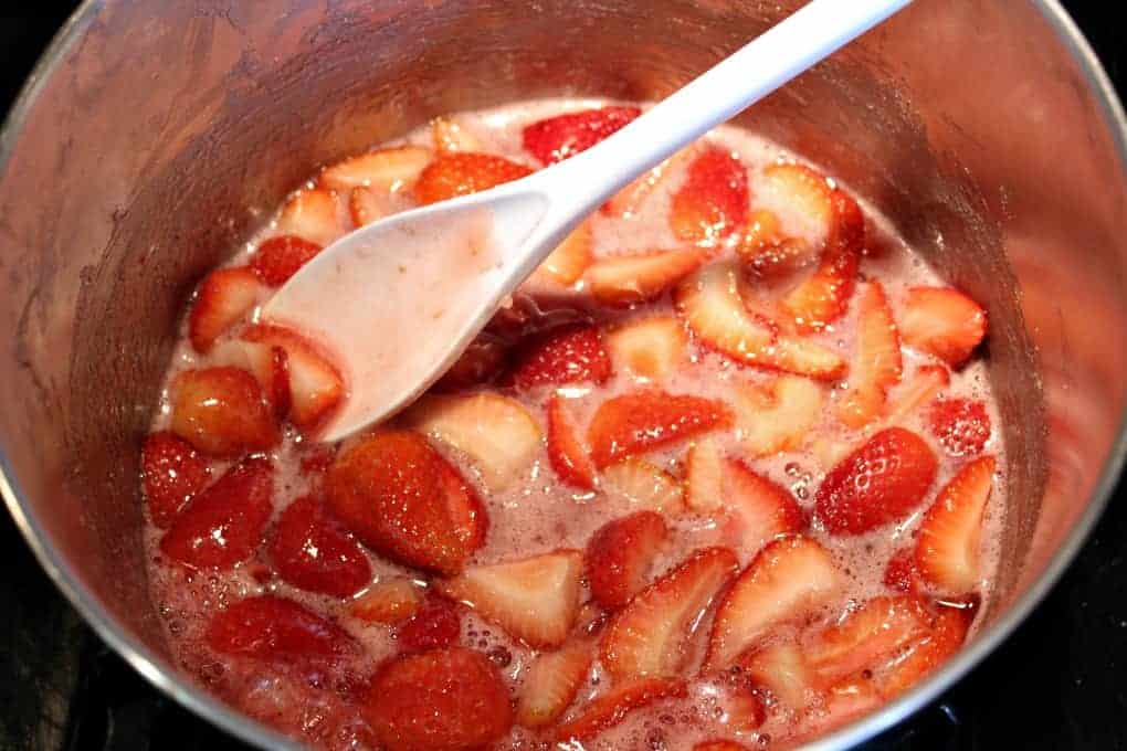 Strawberries cooking in a large pot with a white spoon in the pot.