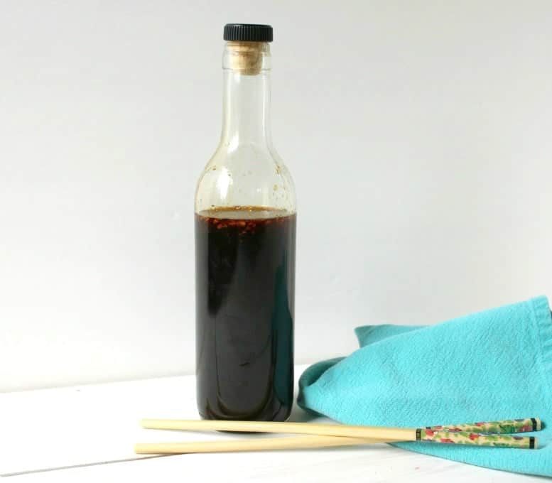 A tall glass bottle partially filled with a dark brown sauce.