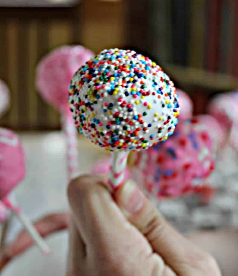 A closeup shot of a white cake pop covered in small colorful sprinkles.