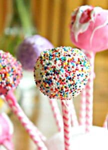 Round balls of cake stuck on a colorful stick and covered with a candy coating.