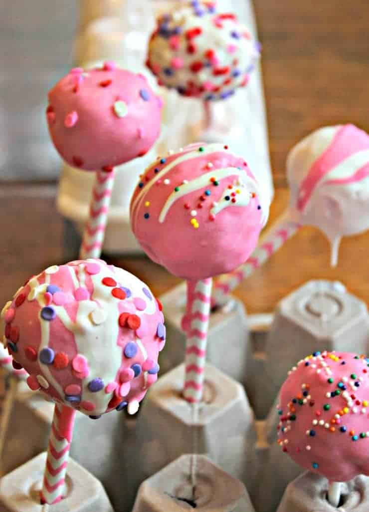 Pink and white cake pops poked into the bottom of an egg carton.