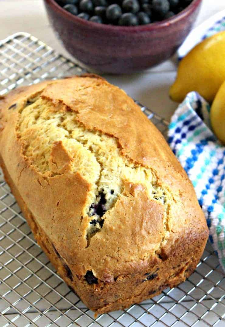 A fresh loaf of blueberry lemon bread cooling on a baking rack.