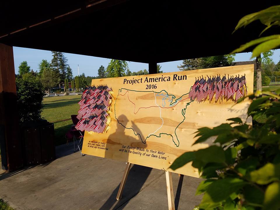 A wooden map on a stand with several small flags on the board.