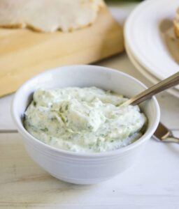 A white bowl filled with mayonnaise with small green flecks of basil.