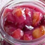 A glass jar filled with cherries in a sauce.