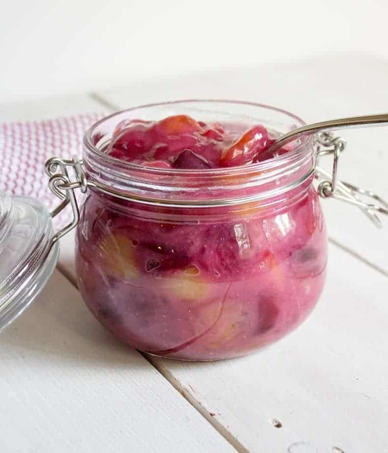 A glass jar filled with cooked cherries.