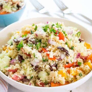 A bowl filled with a couscous salad with fresh veggies and herbs.