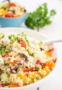 Couscous and fresh veggies in a white bowl with a spoon.