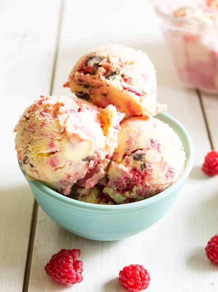 A bowl of ice cream with chocolate and raspberries.
