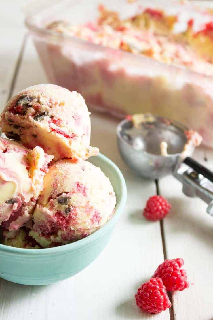 Scoops of ice cream in a small bowl with fresh raspberries next to the bowl.