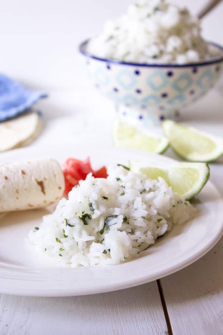 A white plated filled with rice, limes and tortillas.