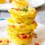 A stack of three mini egg cups filled with cheese, ham and veggies.