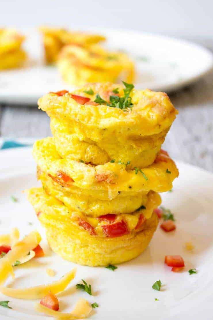 A stack of three mini egg cups filled with cheese, ham and veggies.