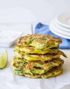 A stack of zucchini fritters on a white surface with a blue napkin behind the stack.