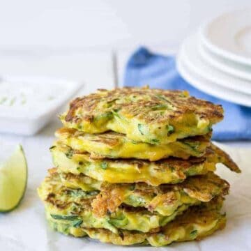 A stack of zucchini fritters on a white surface with a blue napkin behind the stack.