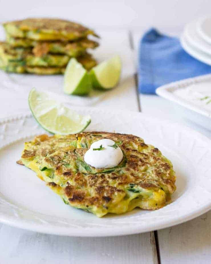 A zucchini pancakes on a plate with a dollop of white cream and fresh cilantro.