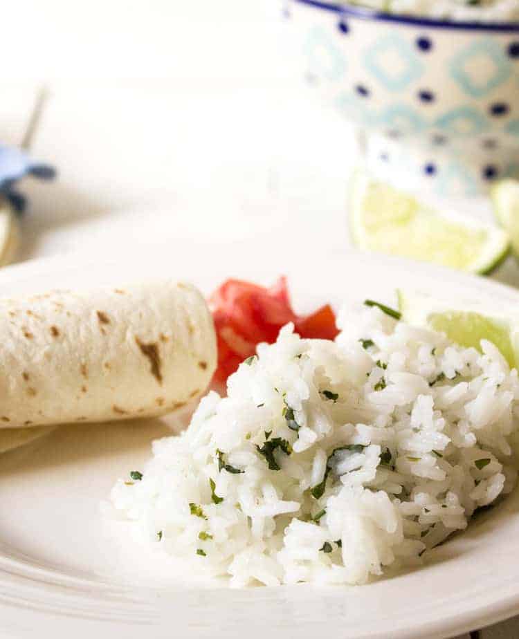 White rice with bits of fresh herbs on a plate with a tortilla and tomatoes.