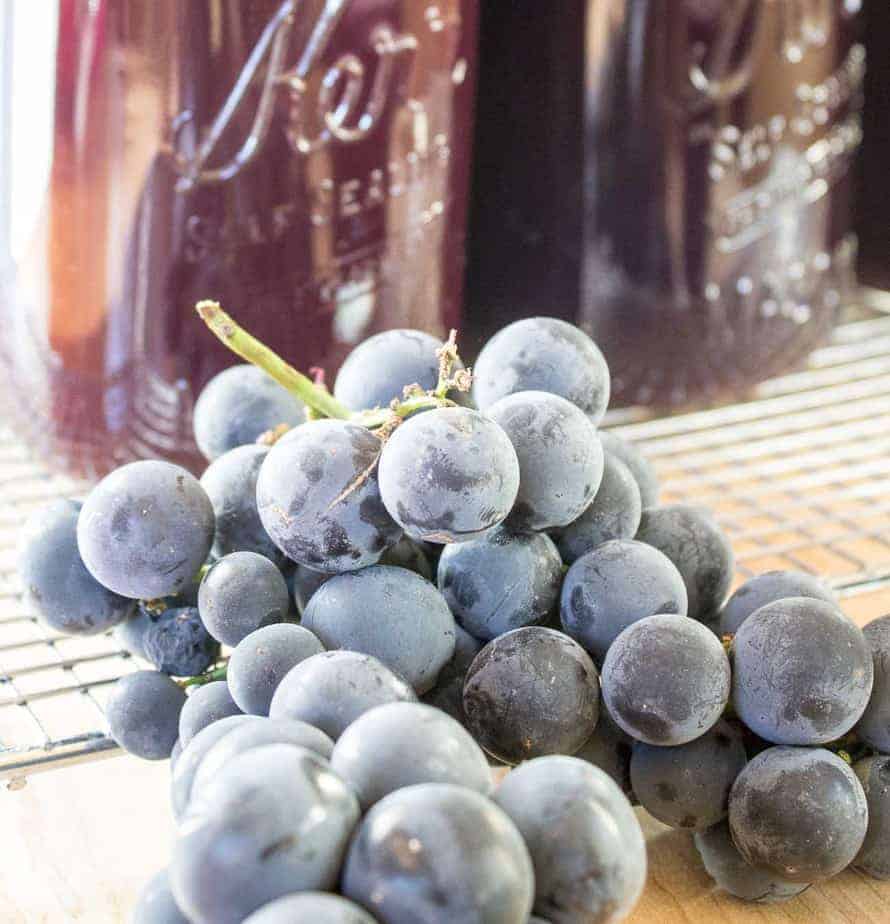 Fresh grapes in front of glass jars filled with juice.