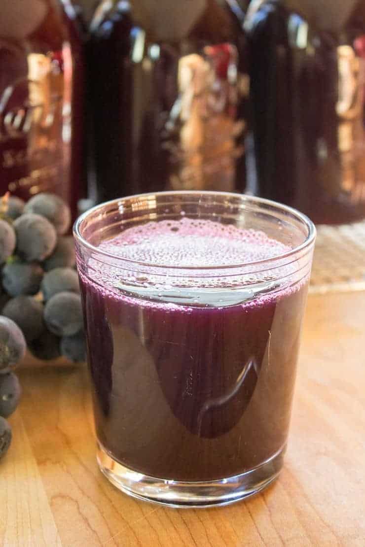 Homemade Grape Juice in a glass with canned juice in the background.