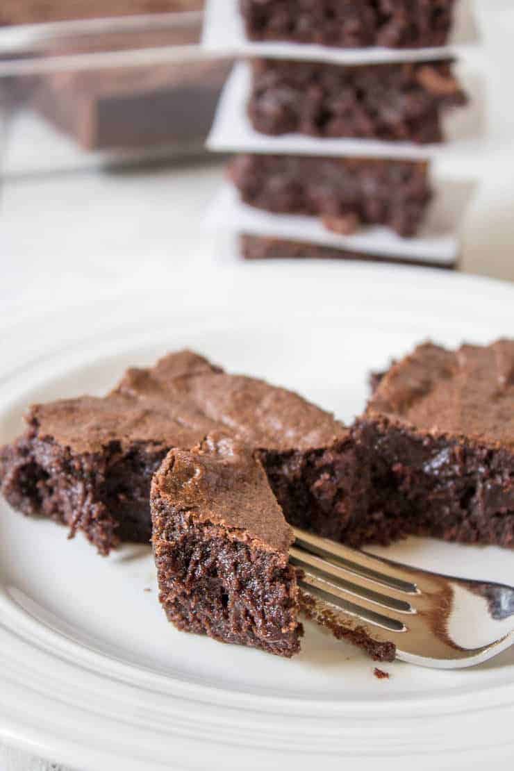 Brownies on a white plate with one piece on a fork. 