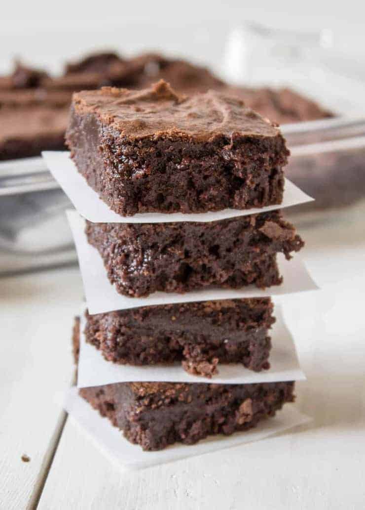 A stack of four brownies with a piece of white parchment paper between each brownie.