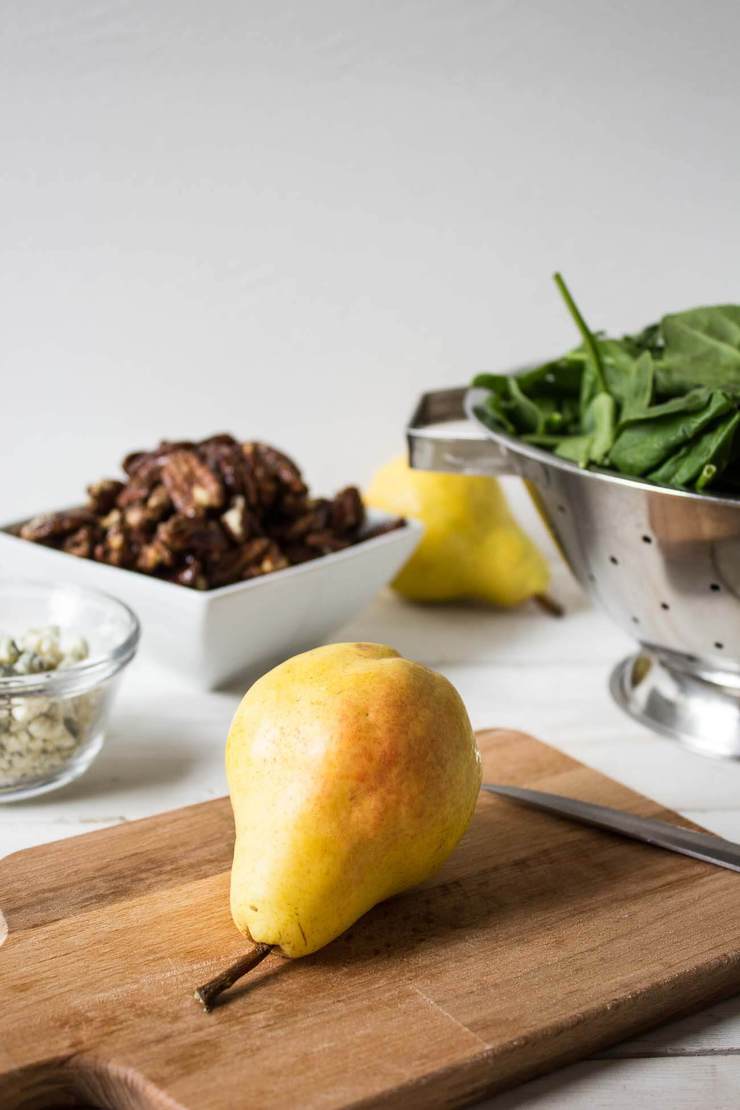 Cutting up a fresh pear on a wooden cutting board with fresh spinach leaves in the background.