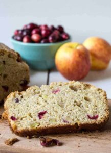 A slice of bread studded with cranberries and apple chunks on a wooden board.