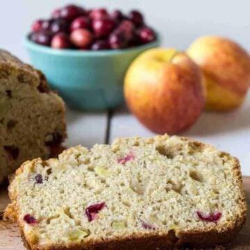 A slice of bread studded with cranberries and apple chunks on a wooden board.