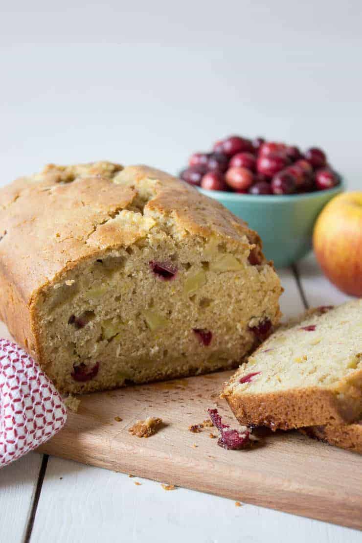 A loaf of bread filled with cranberries and apples on a wooden cutting board.