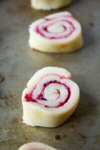 Rolled cookie dough filled with cranberries on a baking sheet.