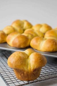A cloverleaf shaped dinner roll on a baking rack with a tray of the rolls in the background.