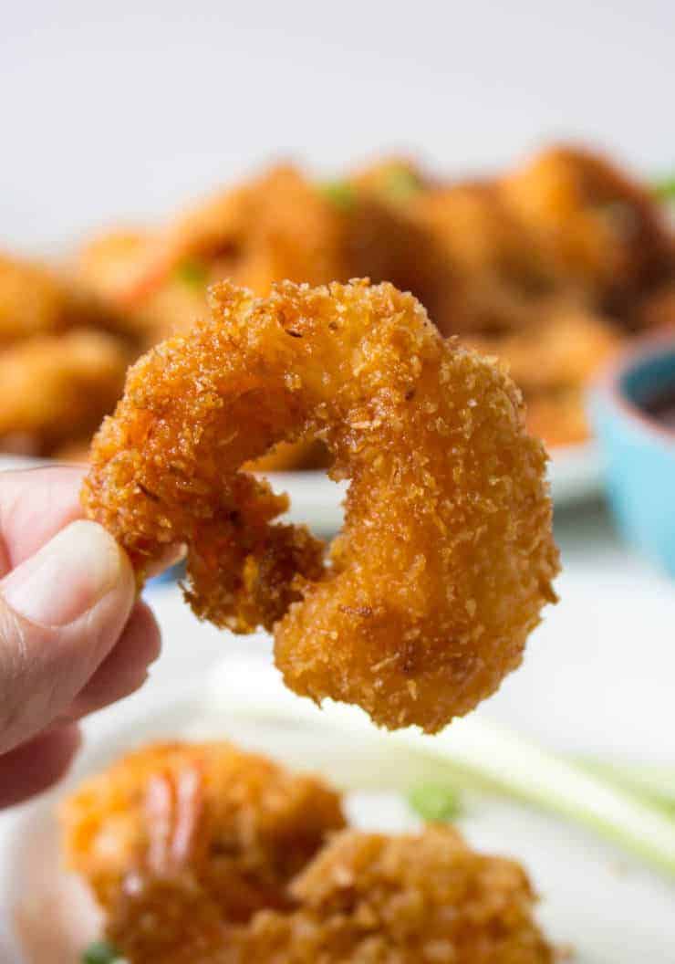 A crunchy shrimp being held in the air above a platter of shrimp.