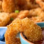 A cooked shrimp with a crunchy coating resting on the rim of a small blue bowl.