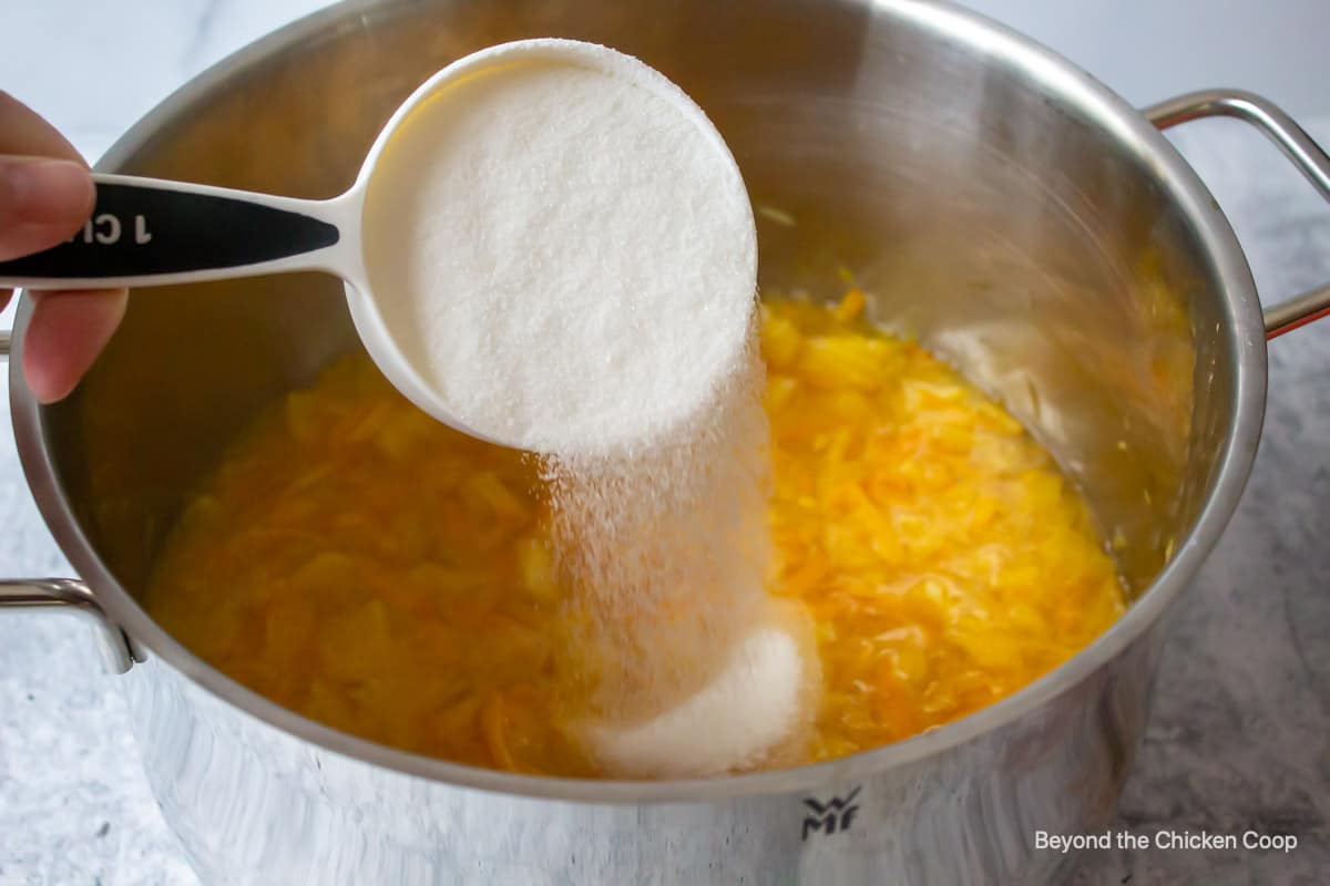 Pouring sugar into a pot with cooked oranges.