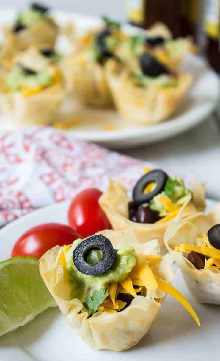 Mini taco shells filled with beans, guacamole, cheese and a black olive.