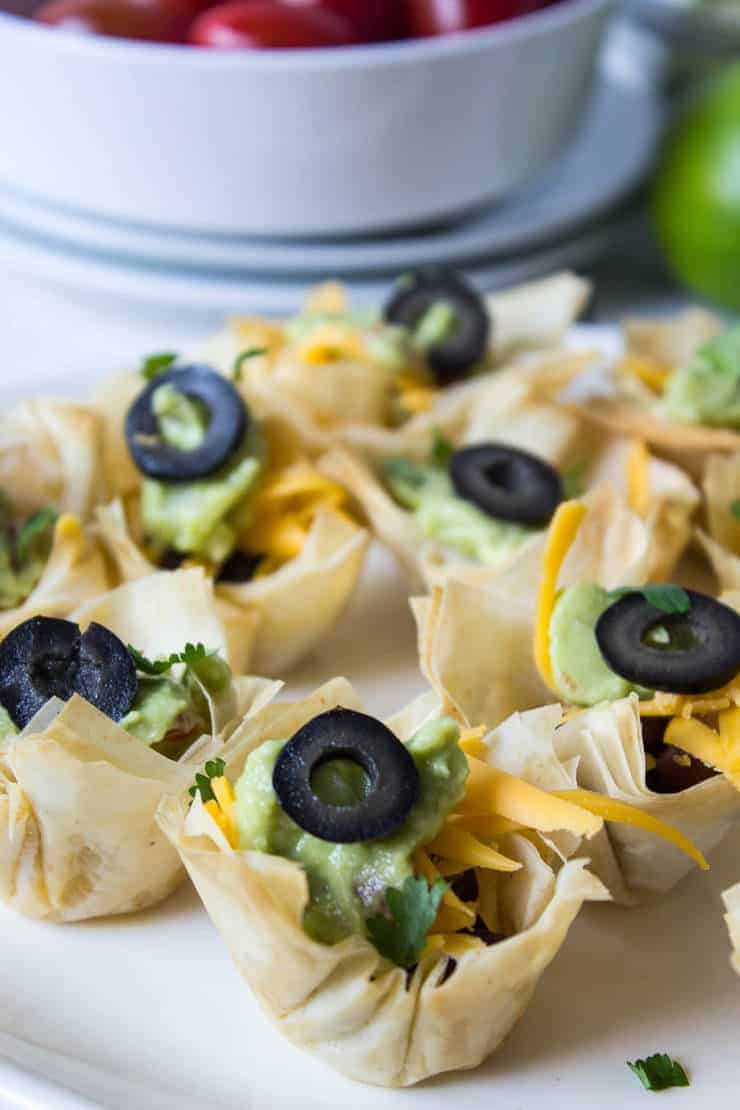 Black Bean Taco Cups filled with cheese and guacamole and topped with a black olive slice.