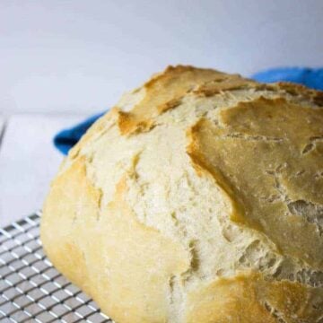 A round loaf of bread with a cracked brown topped on a baking rack.