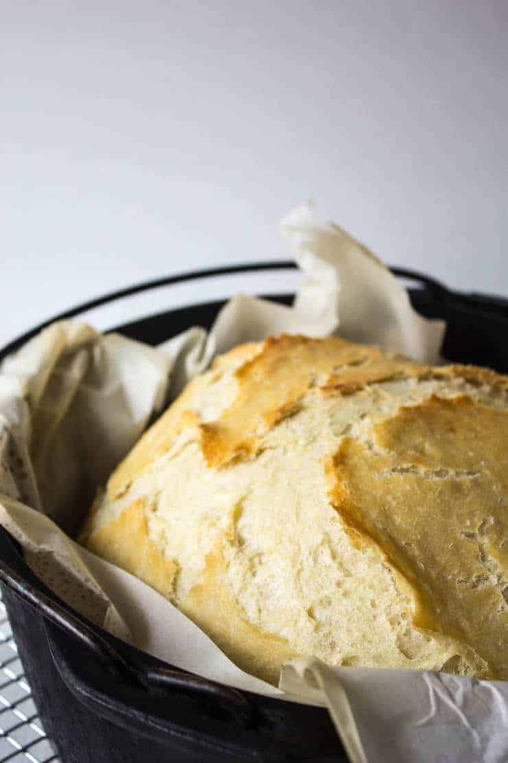 A cooked loaf of bread in a dutch oven pan lined with parchment paper.