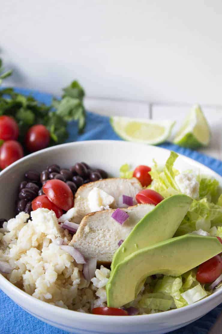 Rice, beans, chicken, lettuce and tomato served in a white bowl.