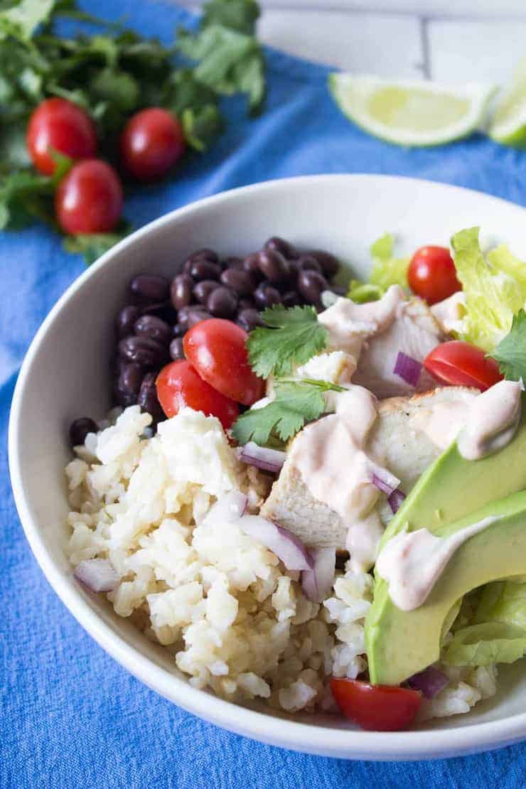 A white bowl filled with black beans, rice, chicken, tomatoes and avocadoes. 