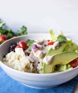 A white bowl with rice, tomatoes, chicken, red onions and avocado slices.