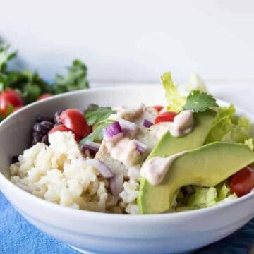 A white bowl with rice, tomatoes, chicken, red onions and avocado slices.