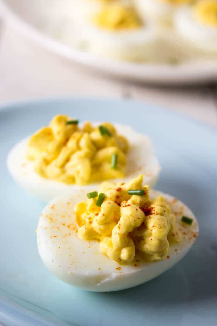 Two deviled eggs on a blue plate with paprika and chives.