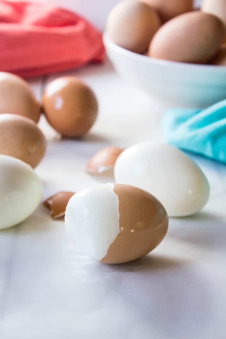 Hard boiled eggs on a white surface with some of the eggs partially peeled.