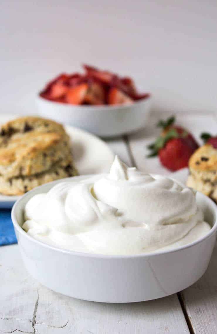 A bowlful of fresh whipped cream and biscuits and strawberries in the background. 