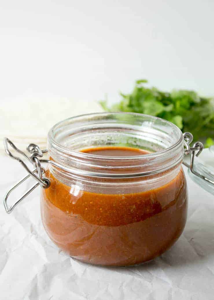 Red sauce in a glass jar with fresh cilantro in the background. 