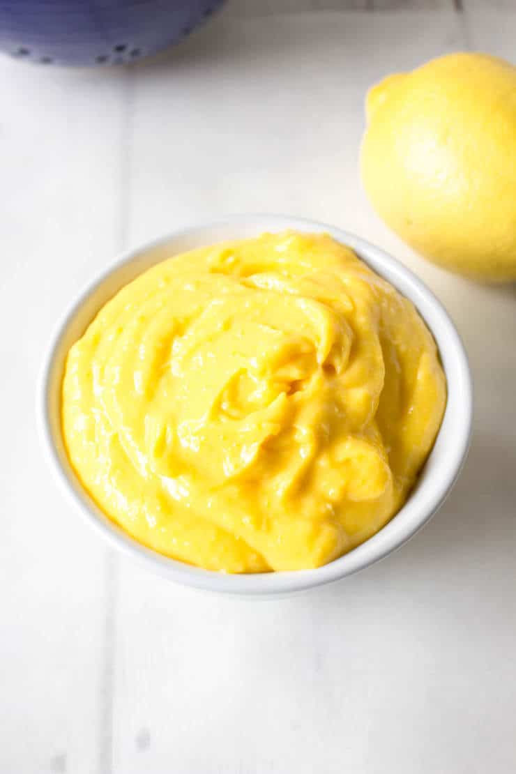 Homemade lemon curd is perfect in a small white bowl on a white board.
