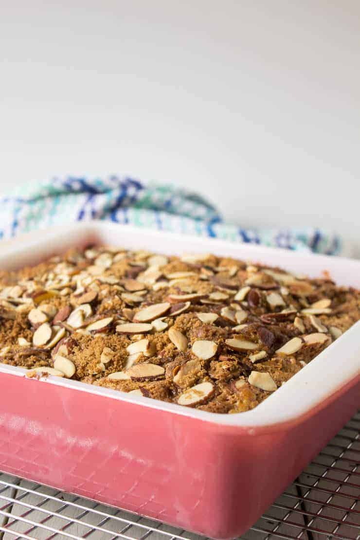 A glass cake dish with a cake topped with sliced almonds. 