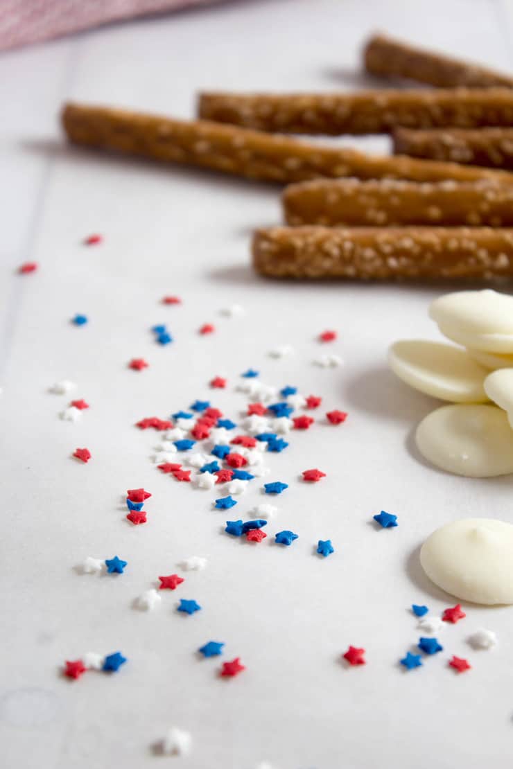 Red, white and blue sprinkles on a board with pretzels rods in the background. 